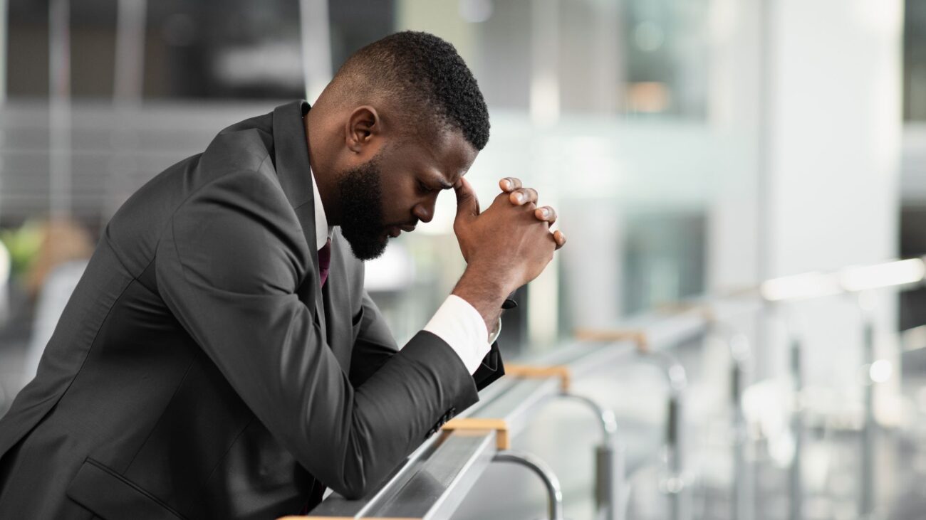 A man in a suit kneels in prayer, symbolizing hope and resilience for Black-owned businesses facing systemic challenges.