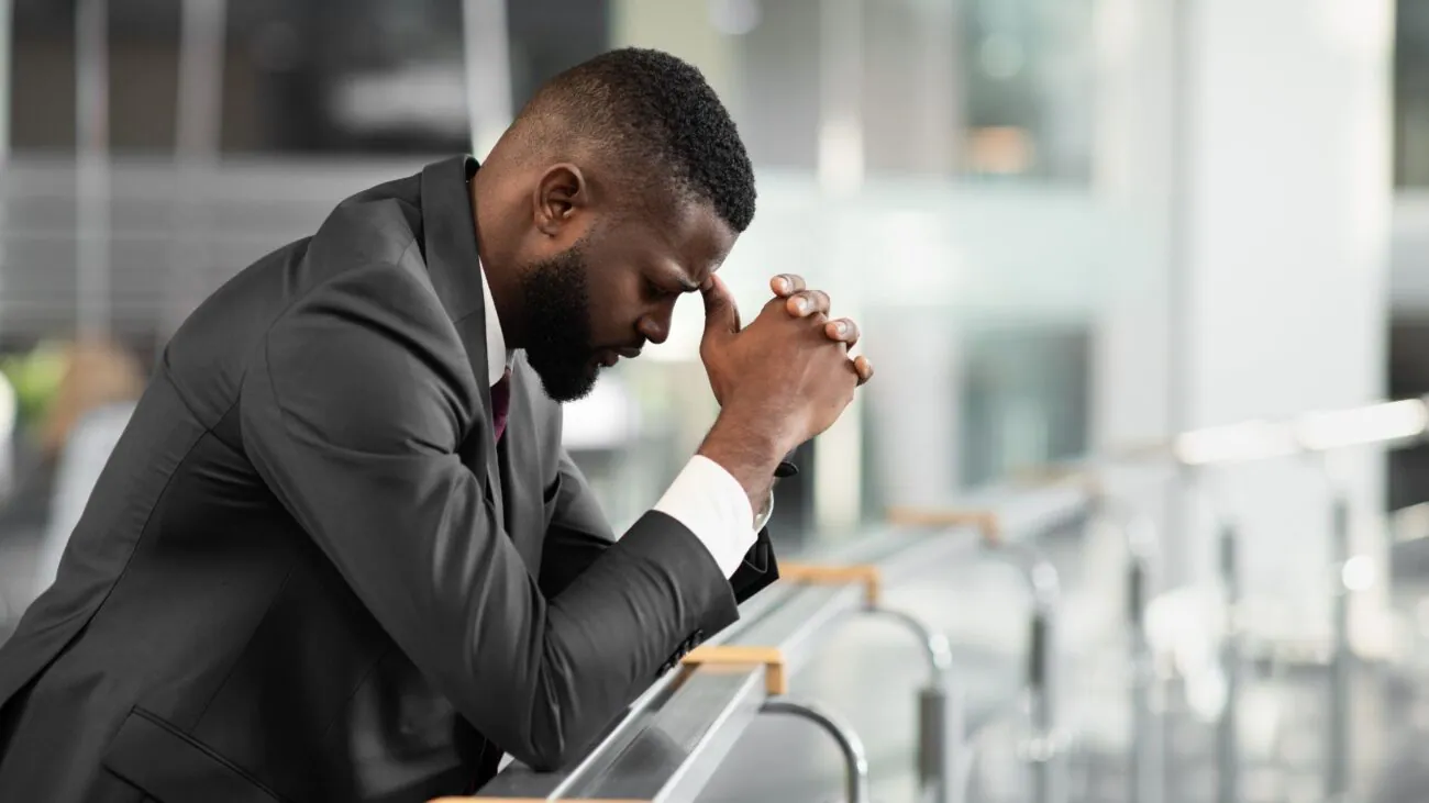 A man in a suit kneels in prayer, symbolizing hope and resilience for Black-owned businesses facing systemic challenges.